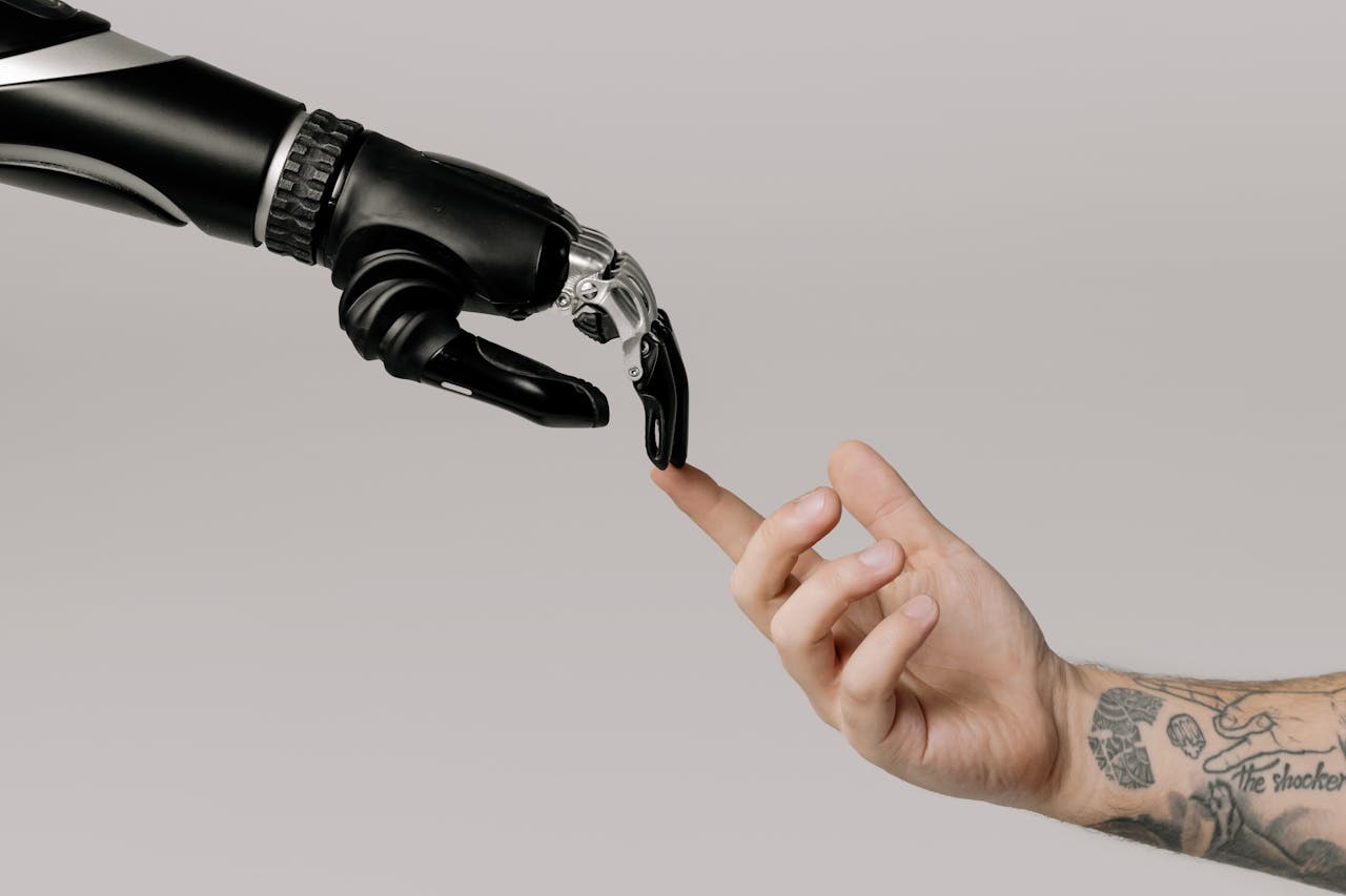 about-01 A human hand with tattoos reaching out to a robotic hand on a white background.